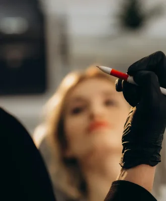 Focused young Asian female cosmetician in black uniform and protective gloves using